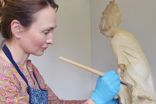 Conservator applying wax to alabaster statute